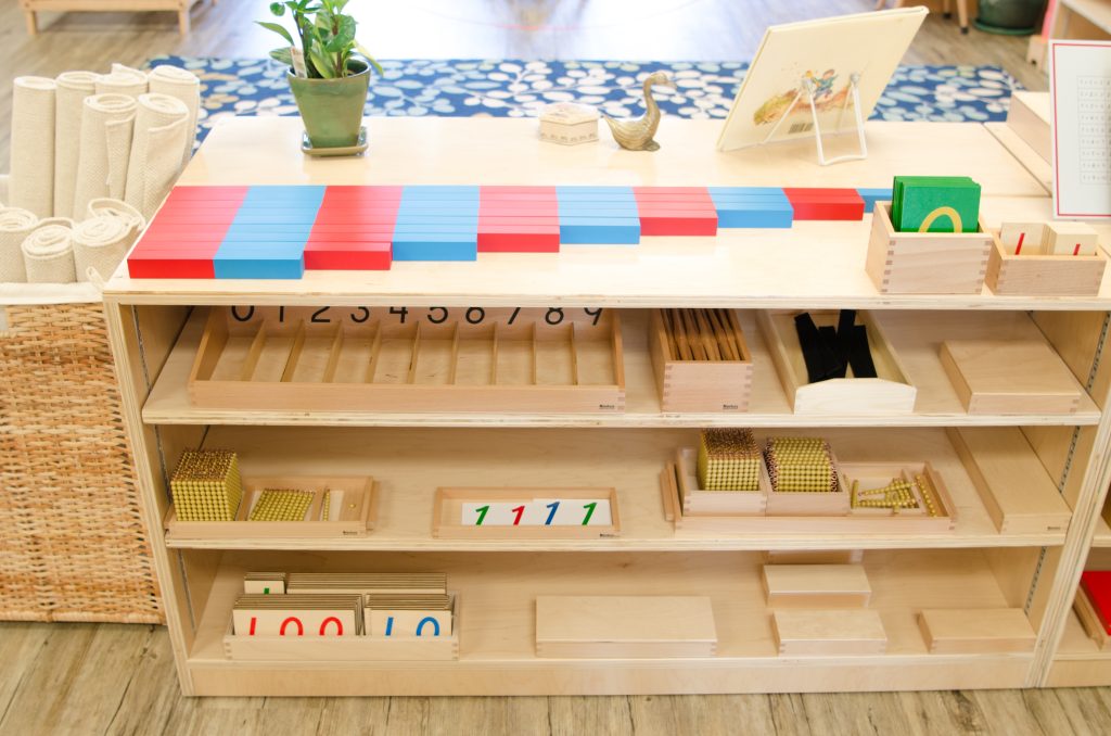 Montessori math shelf with red and blue number rods, golden beads, number cards, and early math work materials.