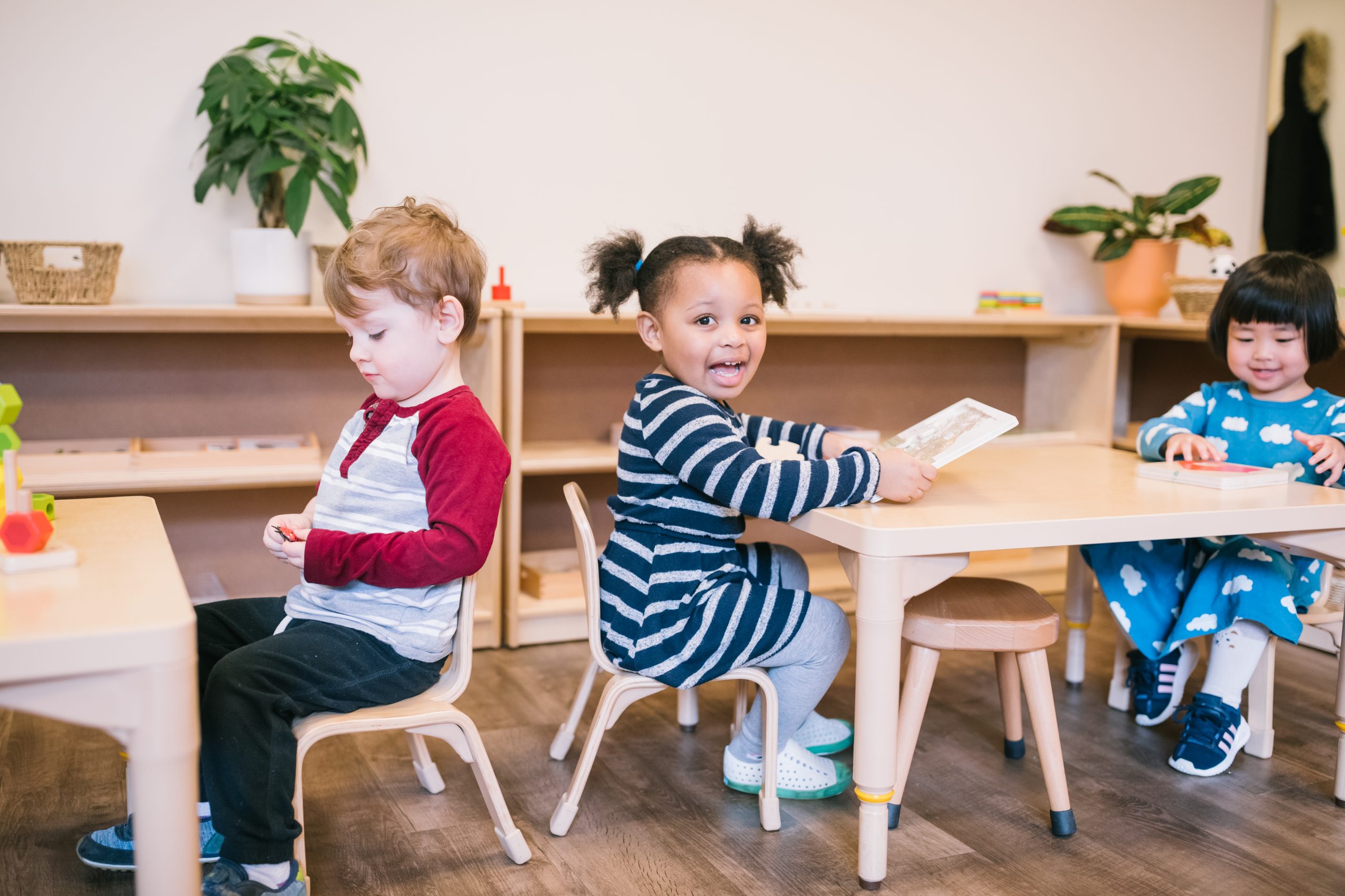 Two toddlers smiling and working together with Montessori materials at a low classroom table. Is My Child Ready for Preschool?