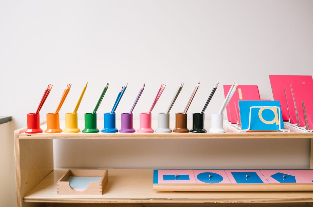 Montessori is expensive writing shelf with colored pencil holders arranged in rainbow order next to metal insets.