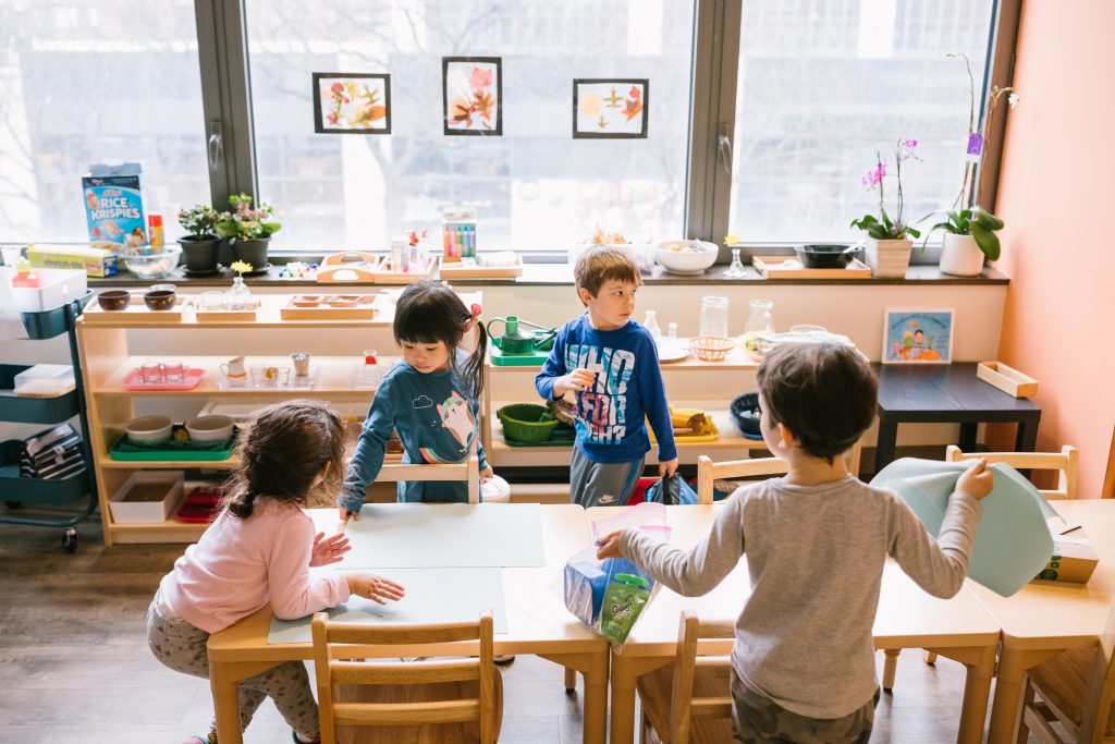 Group of young children engaging with materials at a classroom table in a Montessori environment.