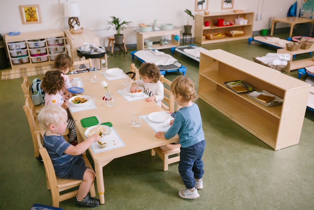 Two toddlers smiling and working together with Montessori materials at a low classroom table.