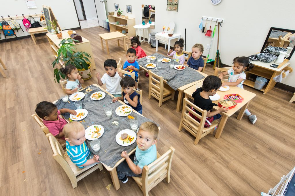 Toddlers share a meal at a child-sized table, practicing self-feeding and independence during the holiday season.
