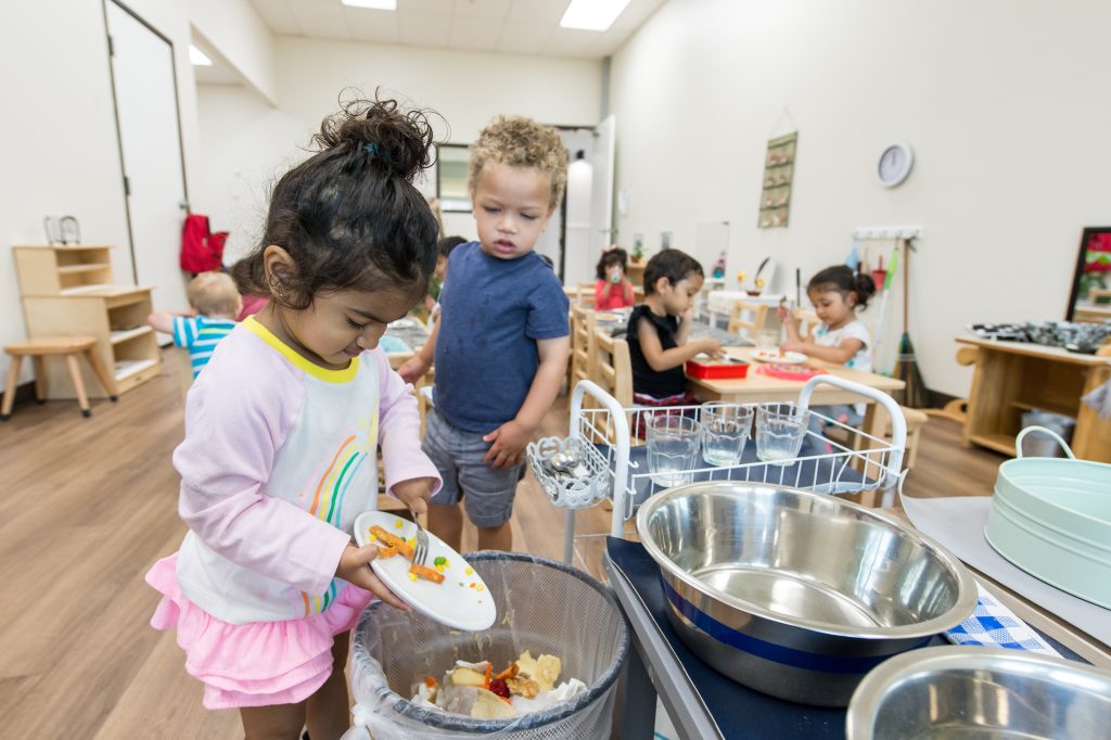 A young child clears their plate after a meal, practicing responsibility in a Montessori classroom during the holidays.