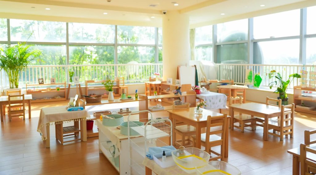 Bright Montessori classroom with wooden shelves, child-sized tables, and large windows bringing in natural light, creating a calm and inviting learning space.