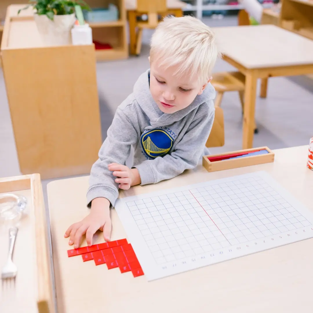Montessori child arranges red math tiles on a number grid at Guidepost Montessori.