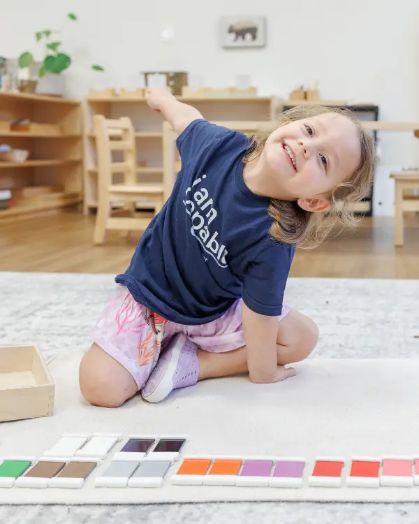 Montessori child smiles while working with color tablets on a rug at Guidepost Montessori.