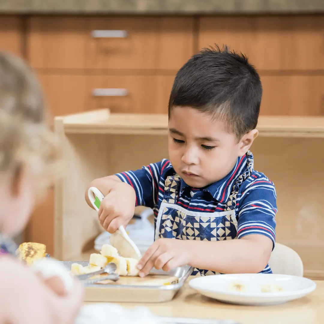 Montessori toddler cuts a banana during a practical life lesson at Guidepost Montessori.